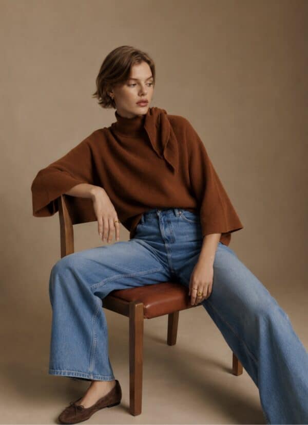 Stylish woman wearing rust cape knit sweater and wide-leg jeans.