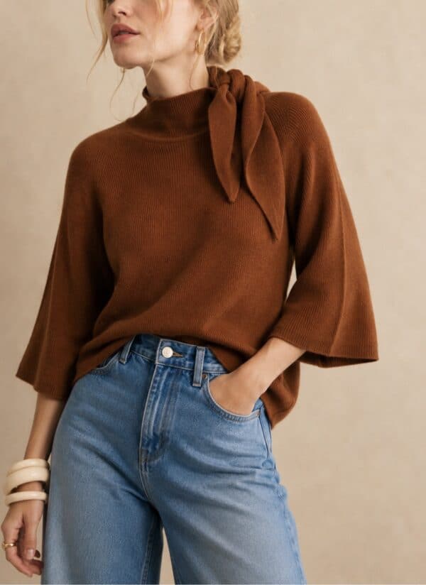 Rust coloured cape knit sweater with tie detail, styled with blue jeans.