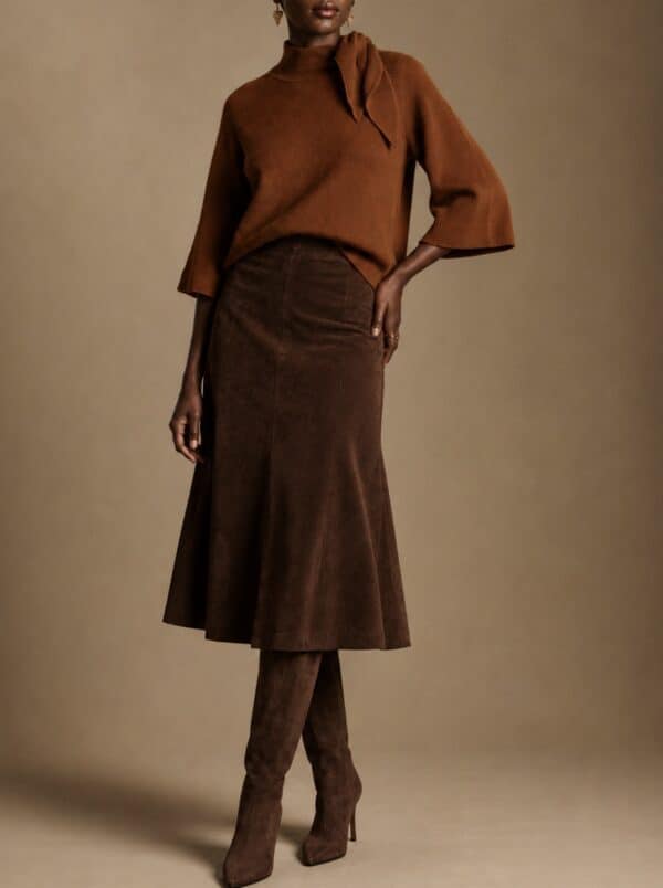 Model wearing a rust-coloured cape knit and matching skirt with boots.