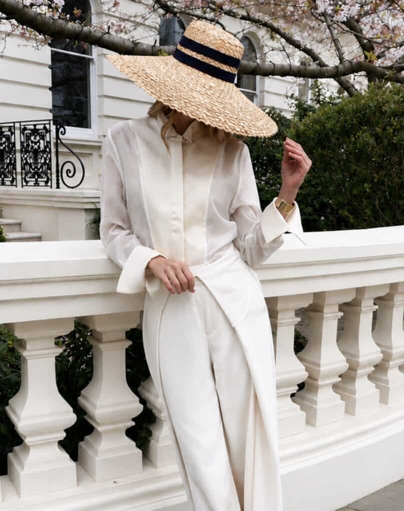Woman in champagne tux shirt with wide-brim straw hat outdoors.