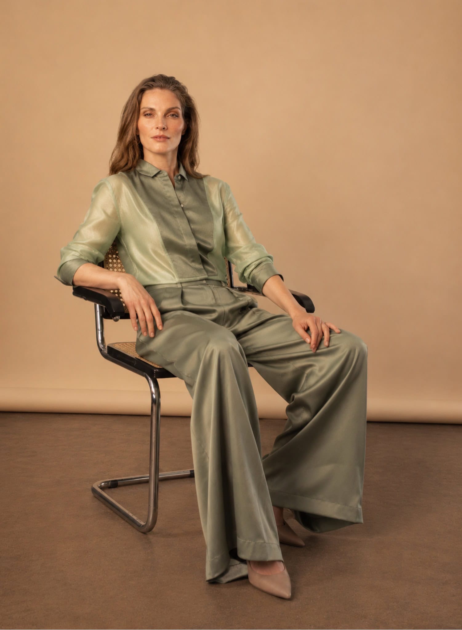 The Sage Tux Shirt 7 sage tux shirt Elegant woman in satin tuxedo and wide-leg trousers, seated on a modern chair.