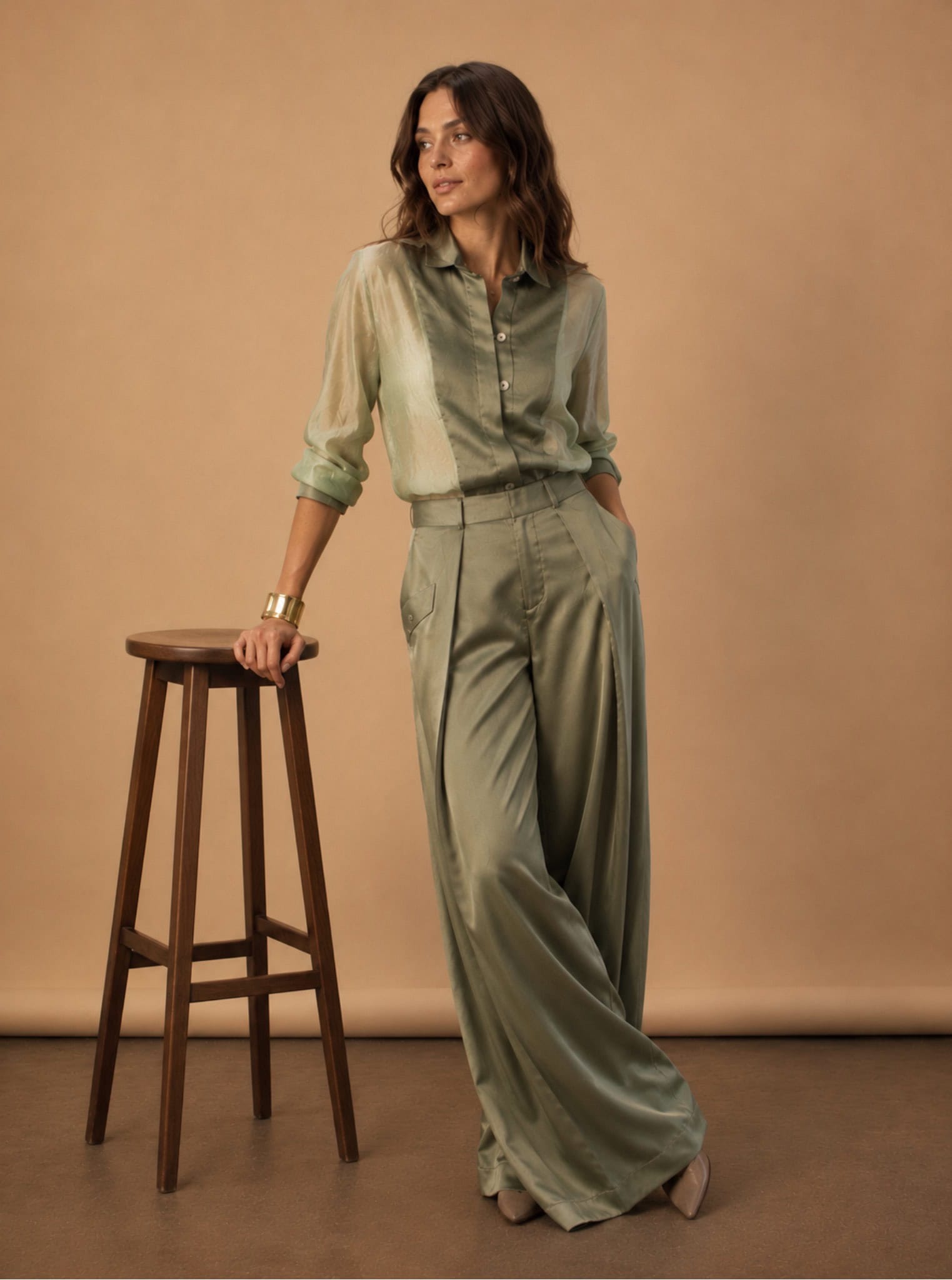 Sage Pleated Palazzo Pant 3 Elegant woman in sage green tux shirt and wide-leg trousers, standing with a stool.