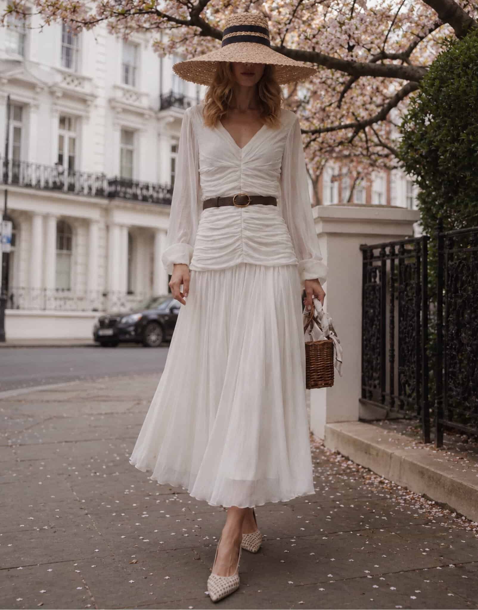 The Audrey 5 champagne tux shirt Woman in white dress with wide-brimmed hat walking in city street.