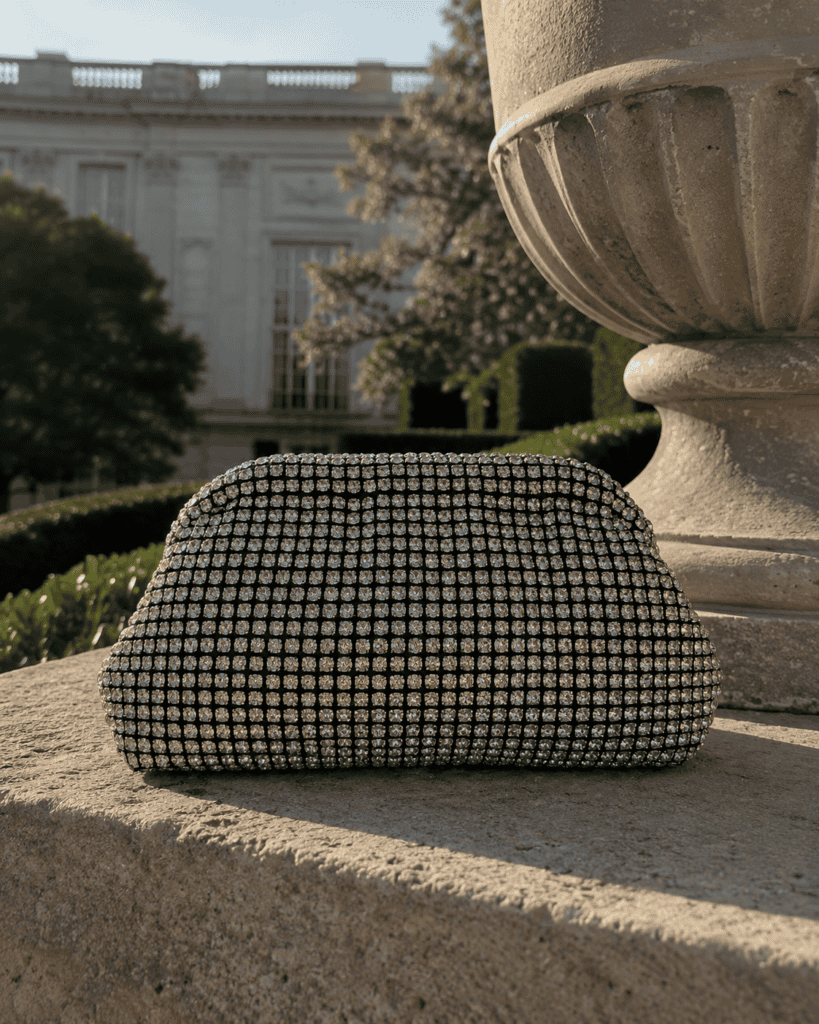 Elegant black clutch bag with gold accents on a stone ledge in outdoor setting.