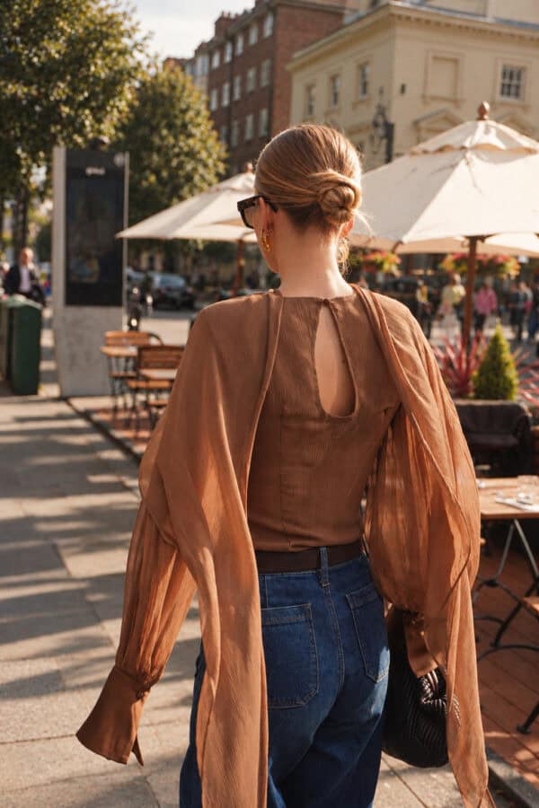 Back view of the tobacco Audrey blouse, showing the keyhole opening and chiffon cape worn with jeans.