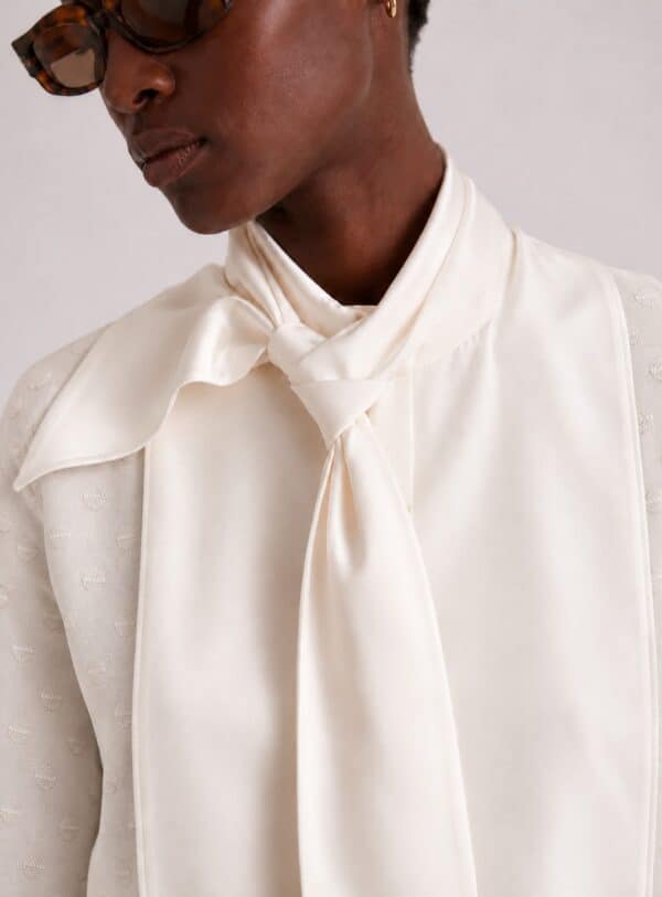 Close-up of the white Gilda shirt's Duchess satin neck tie and rounded bib with woven polka-dot cotton.