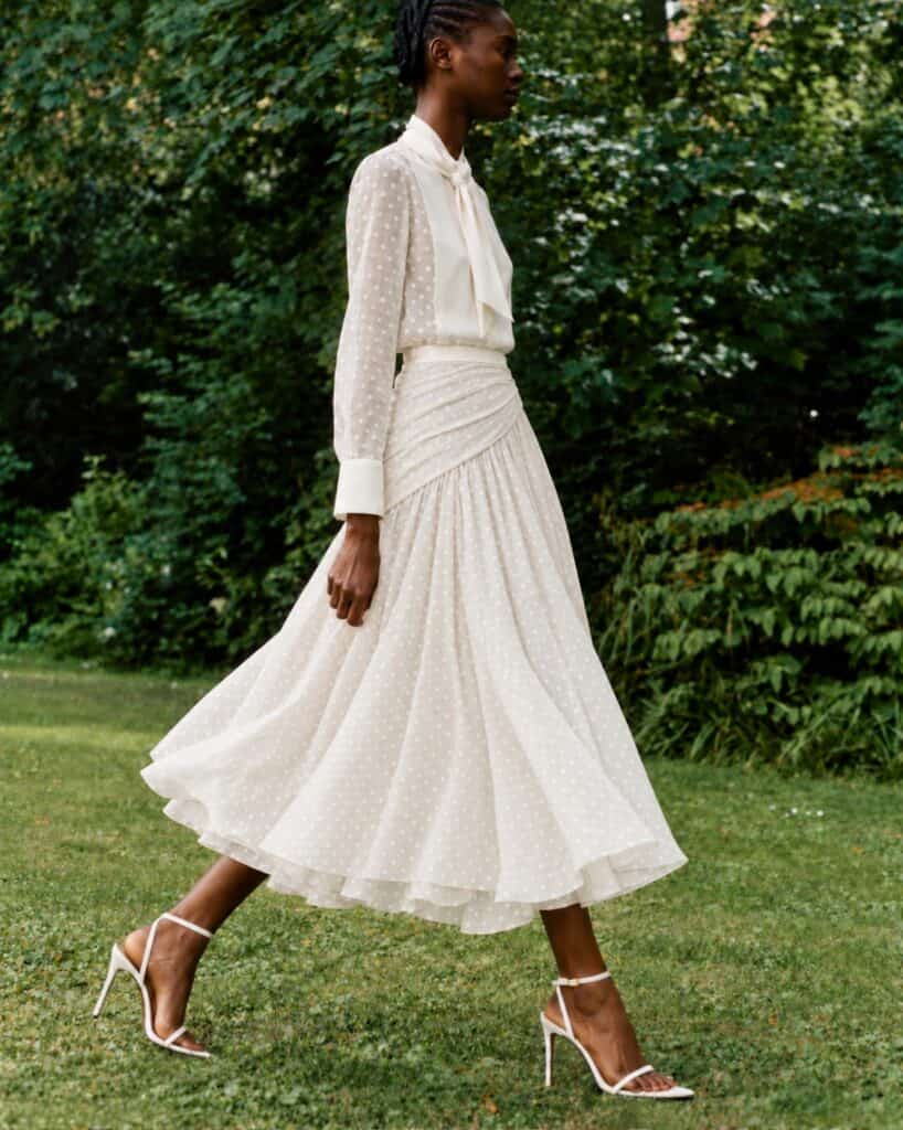 The white limited-edition Gilda shirt and skirt worn walking in a garden, without a handbag.
